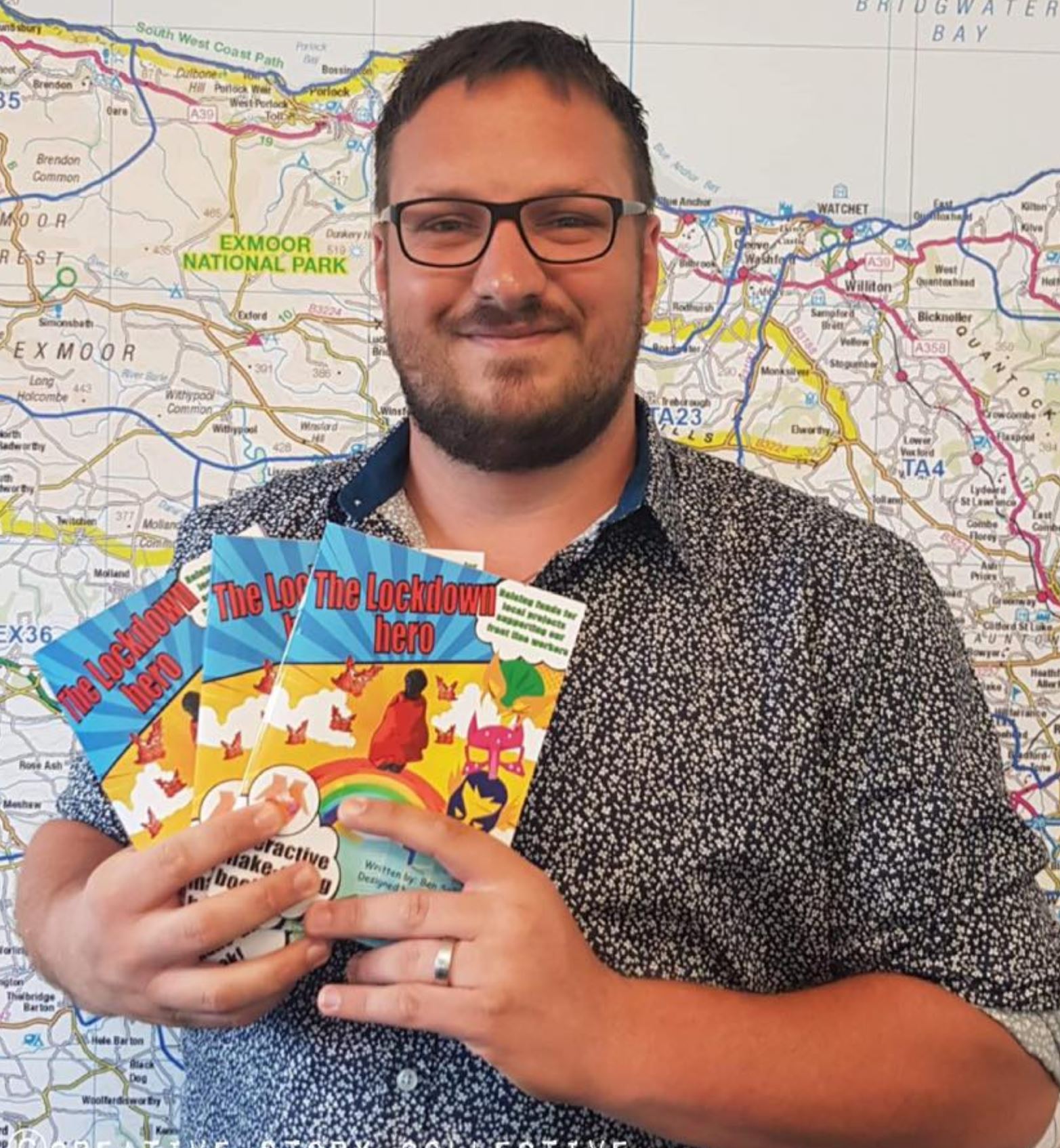 Ben in front of a map holding The Lockdown Hero book